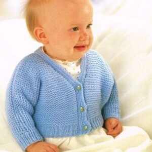 May include: A light blue knitted baby cardigan with a V-neck and button fastening. The cardigan is made with a textured stitch and has a simple design.