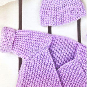 May include: A knitted lavender baby set, including a hat and a sweater. The hat has a small floral detail. The sweater has a folded collar. The set is made of a soft, textured yarn. The items are displayed on a white surface with black stripes.