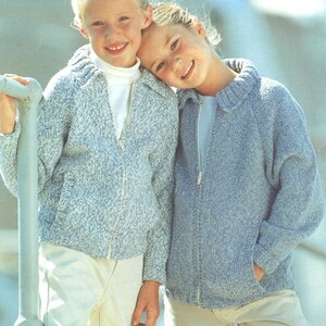 Op de afbeelding: Twee meisjes dragen blauwe en witte gebreide ritsjacks. Het meisje links draagt een wit jack met een blauw patroon. Het meisje rechts draagt een effen blauw jack.