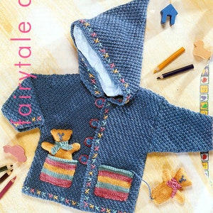 May include: A blue knitted hooded cardigan with a colorful embroidered teddy bear design. The cardigan has a hood and pockets. The cardigan is made of a soft, comfortable material.
