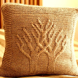 Peut inclure: Un coussin en tricot beige avec un motif d'arbre. Le coussin est fait d'un tissu doux et texturé avec un léger brillant.