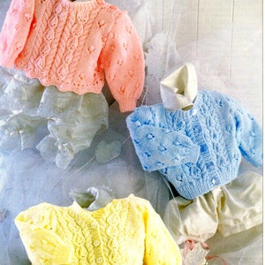 May include: Three knitted baby sweaters in pink, blue, and yellow. Each sweater has a cable knit pattern and button closure.