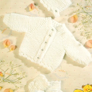 May include: A cream-coloured knitted baby set comprising a cardigan, bonnet, and booties. The set has a textured stitch pattern and decorative edging. The image also includes the text "DOUBLE KNITTING" and "Tiny sizes for early arrivals".
