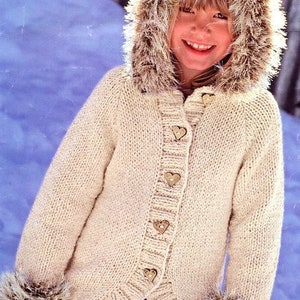 May include: A cream-colored knitted cardigan with a faux fur hood and cuffs. The cardigan has a button closure with heart-shaped buttons.