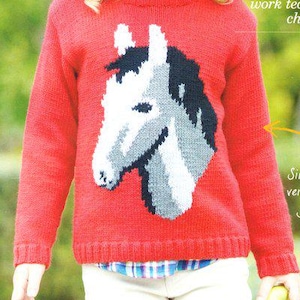 Peut inclure: Un pull rouge en tricot avec un motif de tête de cheval en blanc, gris et noir. Le pull a des manches longues et un ourlet côtelé. La personne porte une chemise à carreaux en dessous et un pantalon blanc.