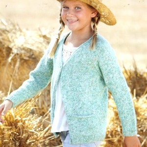 Może przedstawiać: Młoda osoba w jasnozielonym kardiganie z białą koszulą pod spodem i dżinsowymi spodenkami. Nosi słomkowy kapelusz z plecionym wzorem i ma włosy w warkoczach.