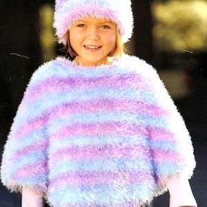 May include: A girl wearing a blue and purple striped fuzzy knit poncho and a matching fuzzy knit hat. The hat is pulled down over her ears. The poncho is a triangular shape and has a wide neckline. The girl is smiling and looking at the camera.