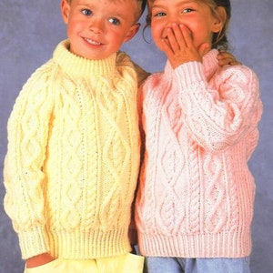 May include: Two children wearing knitted sweaters. The boy is wearing a yellow sweater with a cable knit pattern. The girl is wearing a pink sweater with a cable knit pattern.