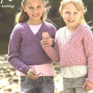 May include: Two girls wearing knitted cardigans with a V-neck and a lace pattern. The cardigan on the left is purple and the cardigan on the right is pink. Both girls are wearing jeans.