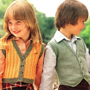 May include: Two children wearing knitted vests. One vest is yellow with green trim and buttons, the other is green with green trim and buttons. Both vests are buttoned up. The children are smiling.