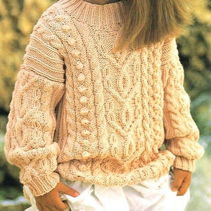 Può includere: Un maglione di colore crema lavorato a maglia con un motivo a treccia e un collo rotondo. Il maglione ha una superficie testurizzata ed è realizzato in un materiale morbido e caldo.