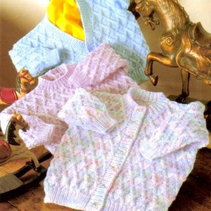 May include: Three knitted baby sweaters in shades of blue and pink. The sweaters have a diamond pattern and are made with a soft yarn.