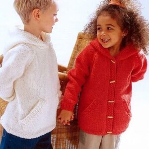 Op de afbeelding: Twee kinderen dragen gebreide hoodies. Het meisje draagt een rode trui en de jongen draagt een witte trui.