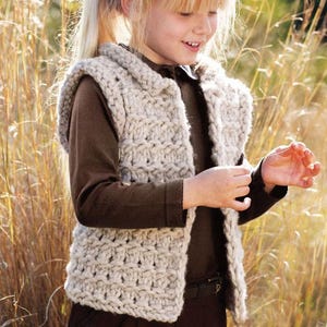 May include: A young girl wearing a white crocheted vest with a hood. The vest has a cable knit pattern and is sleeveless. The girl is standing in a field of tall grass.