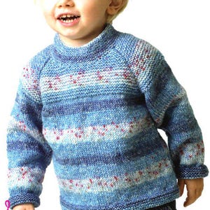 May include: A blue and white knit sweater with a mock turtleneck. The sweater features horizontal stripes in varying shades of blue, white, and red accents. The sleeves and body are a medium length, suitable for a child.