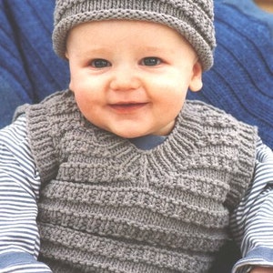 Puede incluir: Un bebé con un chaleco de punto gris y un gorro de punto gris. El chaleco tiene cuello en V y el gorro tiene un diseño sencillo.