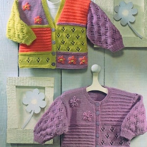 Puede incluir: Dos cárdigans de punto para niños, uno con un diseño de patchwork en verde, naranja y morado con adornos de flores, y el otro de color morado sólido con cierre de botón y adornos de flores.
