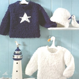 May include: Two knitted baby sweaters, one blue with a white star and one white, hanging on wooden hangers. The sweaters are displayed on a shelf with a white seagull figurine.