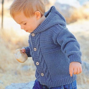 May include: A blue knitted hooded cardigan with button closures. The cardigan has a cable knit pattern and is worn by a young child.
