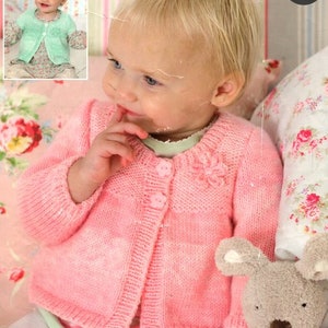 Puede incluir: Un cárdigan de punto rosa con un detalle de flor en la parte delantera. El cárdigan tiene cierre de botón y lo lleva puesto un niño pequeño.