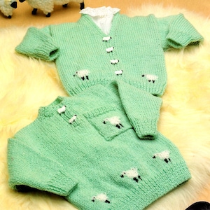 May include: Two knitted baby sweaters in a light green color with a white sheep design. The sweaters have a button closure and are made with a soft yarn.