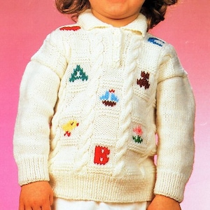 May include: A white knitted sweater with a cable knit pattern and colourful embroidered designs of a boat, a flower, a chick, a triangle, a letter B, and a bear. The sweater has a collared neckline and long sleeves.