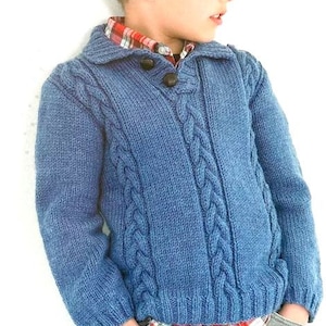 May include: A blue knitted sweater with a cable knit pattern and a button-up collar. The sweater has a red and white checked shirt peeking out from underneath.