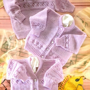 May include: Three lavender knitted baby sweaters with pearl buttons. The sweaters are made with a delicate stitch pattern and have a classic design.