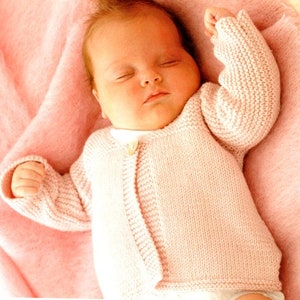 May include: A pink knitted baby cardigan with a button fastening. The cardigan is made from a soft, delicate yarn and has a simple, classic design.