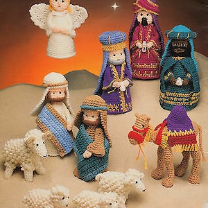 Könnte beinhalten: Eine Sammlung handgefertigter gehäkelter Krippenfiguren, darunter ein Engel, drei Weise, Josef, Maria, Schafe und ein Kamel. Die Figuren sind in verschiedenen Farben gehalten, darunter Weiß, Blau, Lila und Braun. Die Szene spielt vor einem warmen, sonnenuntergangsähnlichen Hintergrund.