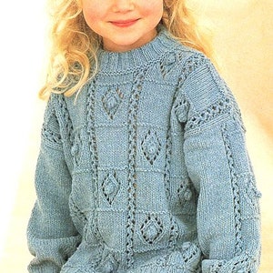 May include: A light blue knitted sweater with a crew neck and long sleeves. The sweater features a diamond pattern and textured details. The cuffs and shoulders have decorative elements. The sweater is made of a soft, possibly wool, material.