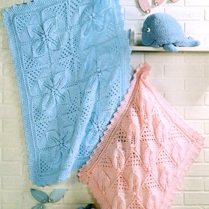 Puede incluir: Dos mantas de bebé de ganchillo, una azul claro y otra rosa, con un delicado patrón floral. Las mantas se muestran en una pared de ladrillo blanco con un juguete de peluche de ballena.