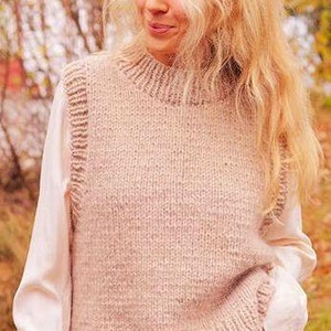 Può includere: Un gilet di maglia marrone chiaro con collo alto e trama a coste. Il gilet è indossato sopra una camicia bianca e jeans blu.