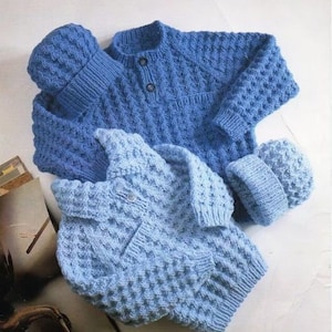 Può includere: Due maglioni blu a maglia e due cappelli abbinati. I maglioni hanno un motivo a maglia testurizzato e chiusure a bottone. I cappelli sono semplici e hanno un bordo a coste.