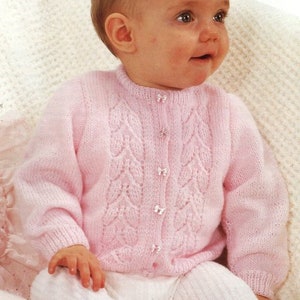 May include: A pink knitted baby cardigan with a button-up front and a delicate leaf pattern. The cardigan has a round neckline and long sleeves.