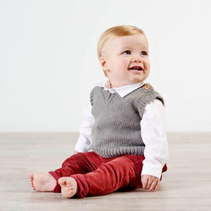 May include: A baby wearing a gray knitted vest over a white collared shirt, paired with red corduroy pants. The baby is sitting on a light wood floor, looking upwards and smiling. The vest has a button detail on the shoulder.