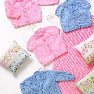 May include: Four knitted baby cardigans in pink and blue with white speckles. Two cardigans have long sleeves and two have short sleeves. The cardigans are laid out on a white surface with decorative pillows.