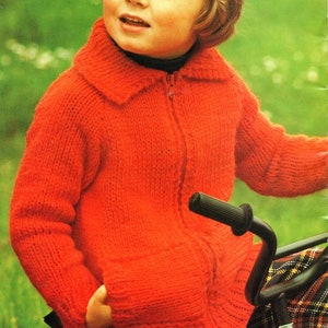 May include: A bright red knitted zip-up jacket with a collared neckline. The jacket has two front pockets and is worn over a black top. The background is a blurred green. The jacket is part of a children's clothing collection.