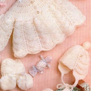 Könnte beinhalten: Ein weißes Strickset für Babys bestehend aus einem Cardigan, einer Mütze und Booties. Der Cardigan hat ein zartes Spitzenmuster und ist 46-48 cm groß. Das Set erfordert etwas Strickkenntnisse.