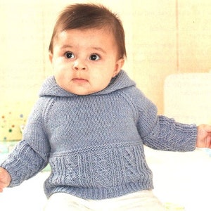 Może przedstawiać: Dziecko w jasnoniebieskim dzianym swetrze z kapturem i wzorem warkocza.