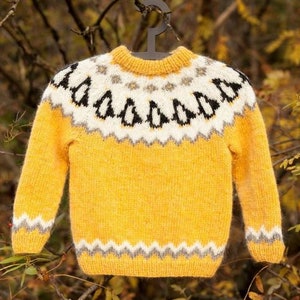 May include: A yellow knitted sweater with a white and black geometric pattern around the neck. The sweater has a fuzzy texture.