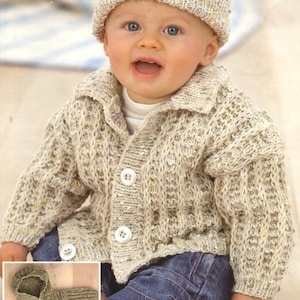 Pode incluir: Um bebê vestindo um casaco de tricô bege com botões e um chapéu de tricô combinando. O casaco tem gola e o bebê está vestindo jeans azul.