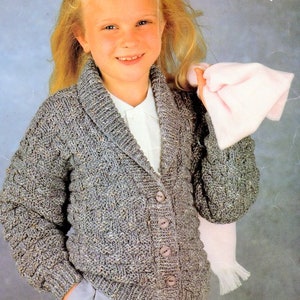 Peut inclure: Une fille portant un cardigan en tricot gris avec un col et une fermeture à boutons. Le cardigan a un motif texturé et est fait de laine épaisse. La fille tient une écharpe rose dans sa main droite. Le texte "Easy knit" est visible dans le coin supérieur droit de l'image.