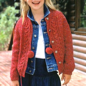 May include: A red knitted cardigan with a cable knit pattern and pom-poms. The cardigan has a button closure and is worn over a white shirt and a denim jacket.
