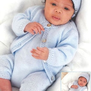 May include: A baby wearing a light blue knitted cardigan and matching pants with a light blue knitted hat. The baby is lying on a white blanket.
