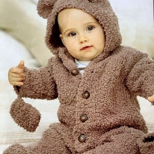 May include: A brown knitted baby bear jumpsuit with a hood and bear ears. The jumpsuit has a button closure down the front and is made of a soft, fuzzy yarn. The jumpsuit is suitable for a baby from birth to 2 years old.