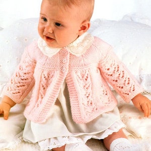 May include: A pink knitted baby cardigan with a white lace collar. The cardigan has a delicate cable knit pattern and is worn by a baby sitting on a white blanket. The text "43-48 cm 17-19 in. Three sizes" is visible in the top right corner of the image.