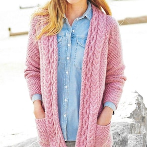 May include: A light pink, open-front cardigan with a cable knit design along the front and sleeves. The cardigan has two front pockets and is worn over a blue denim shirt. The sleeves are long, and the cardigan appears to be made of a soft, textured yarn.
