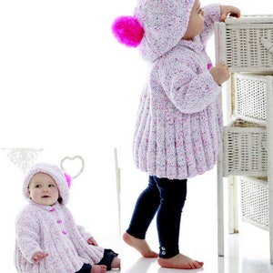 May include: A white and pink knitted baby jacket with a hood and a pink pom-pom. The jacket has a button closure and is being worn by a baby.