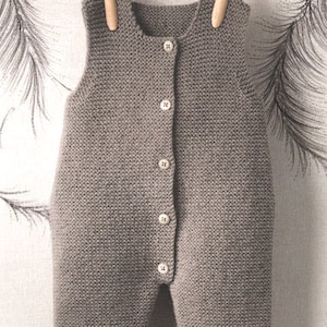 Op de afbeelding: Een grijze gebreide baby romper met witte bies aan de benen en een knoopsluiting aan de voorkant.